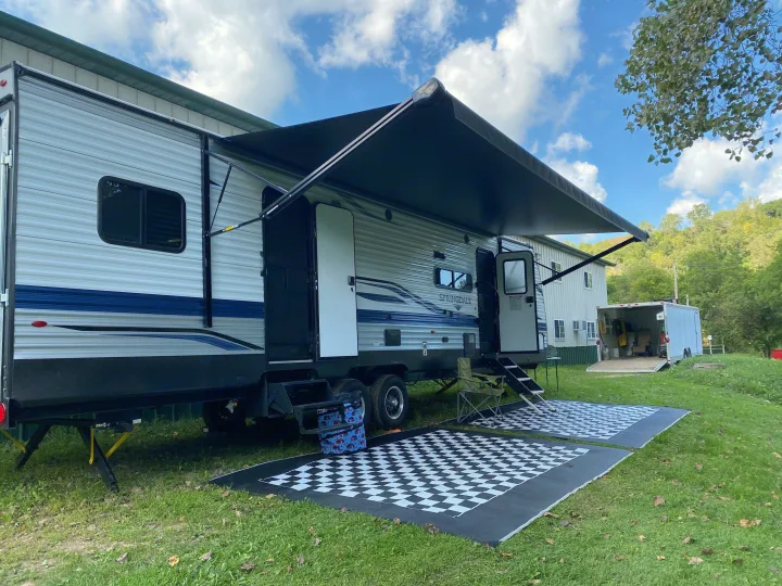 Spacious RV rental set up with an awning & checkered outdoor mats, ready for a relaxing getaway.. Keystone Springdale 2021