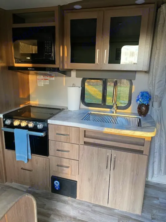 Our RV rental kitchen features light wood cabinets, microwave, stove/oven, and counter space with a sink.. Grand Design 21BHE 2023