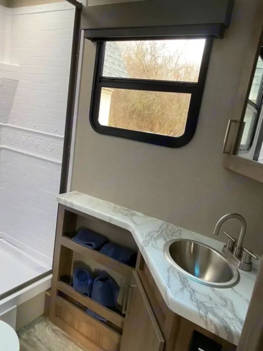 Modern RV rental bathroom with vanity, sink, open towel storage, and a scenic window view.. Grand Design 21BHE 2023