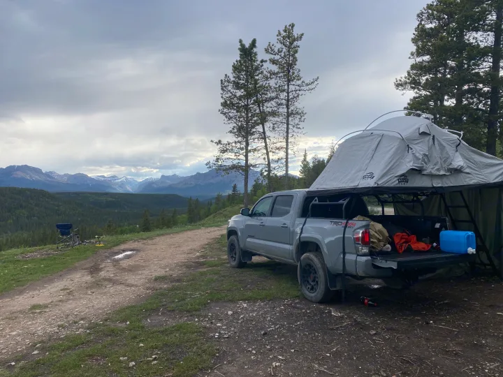 Grey truck with rooftop tent for camping & overlanding, parked before mountains. An 'rv rental' alternative for adventure seekers.. Toyota Tacoma 2020