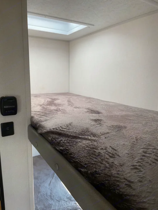 Inside an RV rental: a cozy bunk bed with a soft gray blanket, overhead light, and climate controls.. Avenger LT 2022