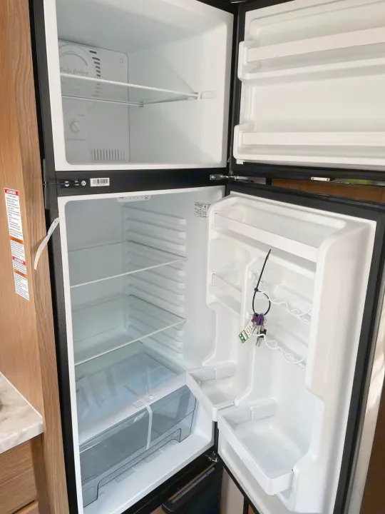 Empty, clean two-door RV rental fridge with freezer on top, ready for your trip. Keys hanging inside.. Avenger LT 2022