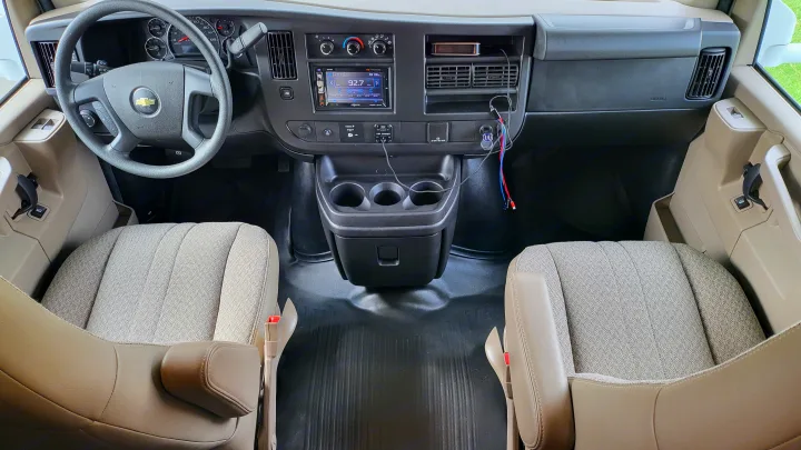 Chevrolet RV rental's spacious front cabin, featuring a detailed dashboard, steering wheel, digital radio display (92.7 FM), and comfortable front seats.. Thor 22HE 2019