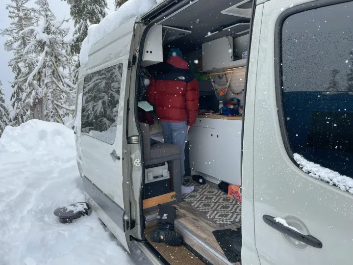 Cozy RV rental in a snowy forest. A person is inside the camper van, highlighting mobile winter living.. Mercedes-Benz Sprinter 2018