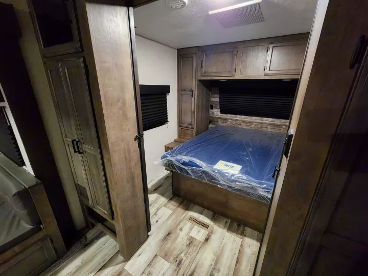 Inside an RV rental: a cozy bedroom with a new Serta bed, built-in cabinets, and wood-look flooring.. Venture Sporttrek 2022