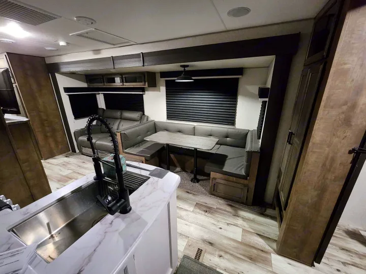 Inside a modern rv rental: kitchen counter, sofa, and U-shaped dinette in a light wood and gray interior, designed for comfort.. Venture Sporttrek 2022