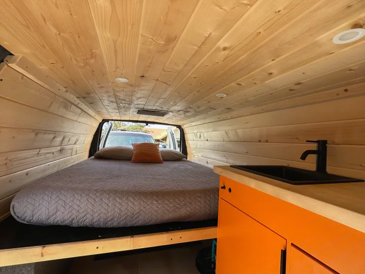 Cozy RV rental interior with wood paneling, comfortable bed, and compact kitchen area.. Ford Extended E350 2011