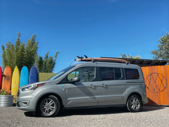 This Ford Transit Connect RV rental, equipped with a surfboard, is ready for beach adventures by colorful boards.. Ford Transit Connect Wagon 2022