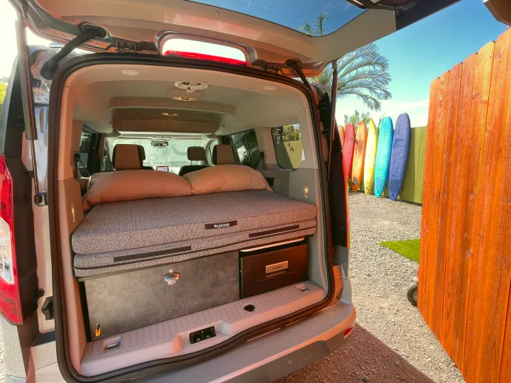 Compact camper van RV rental setup with cozy bed, storage, and fridge, perfect for surf adventures!. Ford Transit Connect Wagon 2022