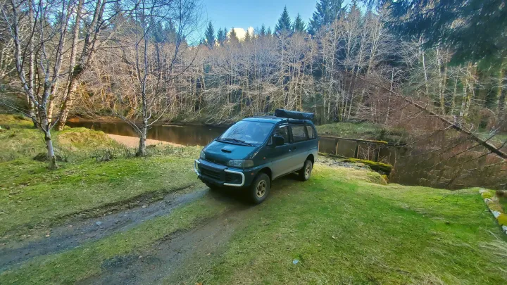 Teal 4x4 camper van parked by a river in a forest, ready for an rv rental adventure in the wilderness.. MITSUBISHI Delica 1997