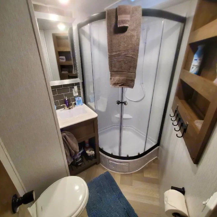Explore this compact RV rental bathroom featuring a corner shower, sink vanity, toilet, and shelving for essentials.. Forest River Salem 2022