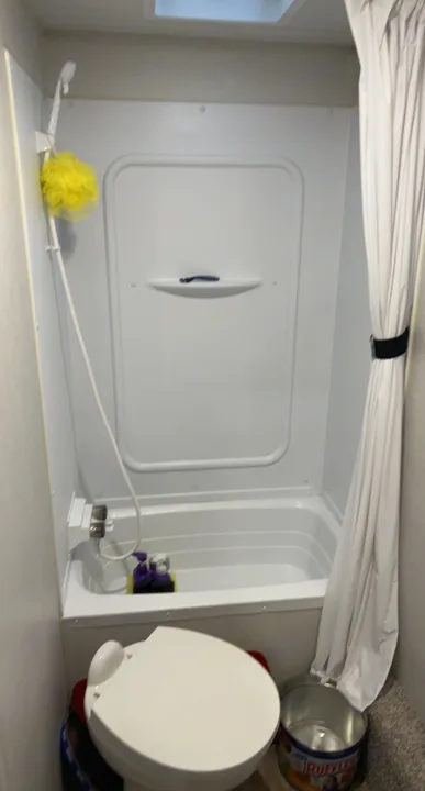 View of a compact bathroom inside an RV rental, featuring a small bathtub/shower unit, toilet, and shower curtain.. Keystone RV Hideout 2022