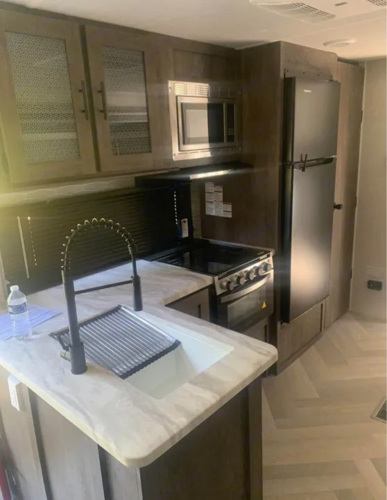Bright RV rental kitchen with modern black faucet, sink, stovetop, microwave, and fridge. Stylish cabinets and ample counter space.. Forest River Salem 2021