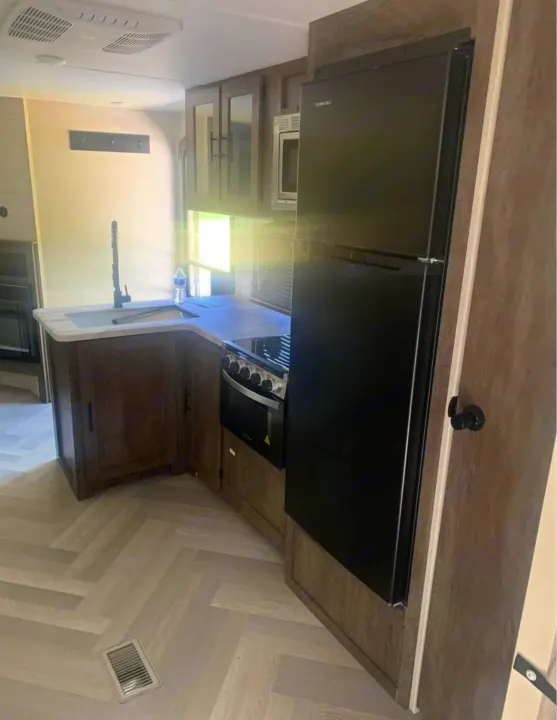 RV rental's modern kitchen: black fridge, stove, sink, and herringbone floor. A functional, compact space for travel.. Forest River Salem 2021