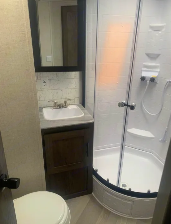Compact RV rental bathroom features a sink, mirror, toilet, and corner shower, optimizing space for travel comfort.. Forest River Salem 2021