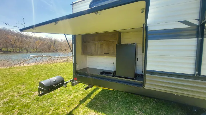 This RV rental features a convenient outdoor kitchen with a sink, fridge, and attached grill, perfect for riverside camping.. Forest River Wildwood 2020
