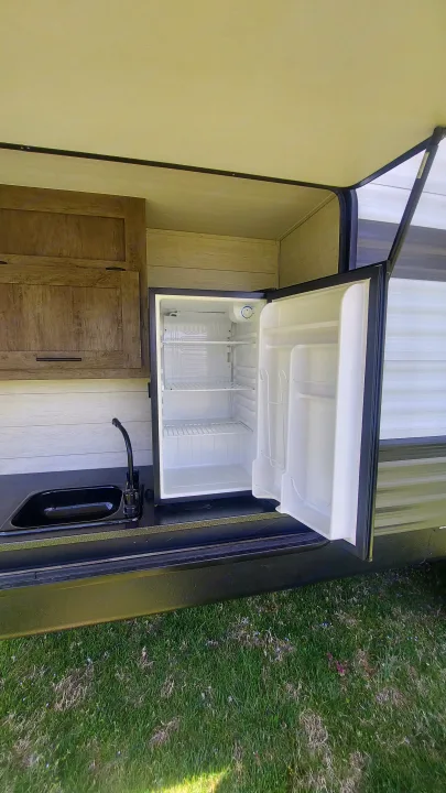 Explore this RV rental's outdoor kitchen: a mini-fridge with open door, sink, and cabinets for convenient camping.. Forest River Wildwood 2020
