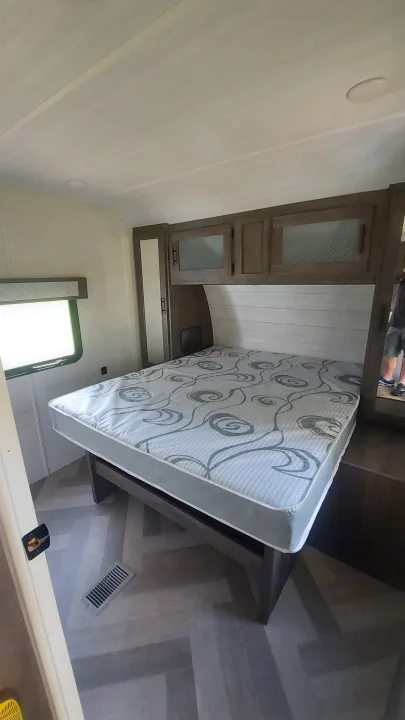 Explore this RV rental's compact bedroom with a patterned mattress, dark wood cabinets, and modern flooring.. Forest River Wildwood 2020