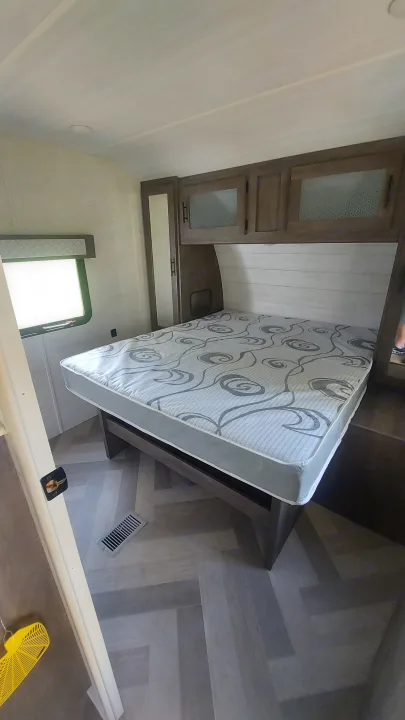 RV rental bedroom: cozy space featuring a patterned mattress on a raised platform, wood cabinets, and herringbone flooring.. Forest River Wildwood 2020