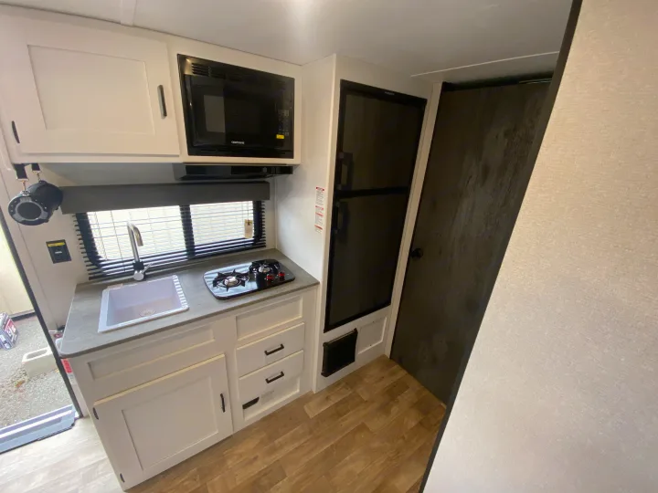 RV rental kitchen: bright interior with white cabinetry, sink, stove, microwave, and refrigerator. Essential amenities for travel.. Keystone Hideout 2022