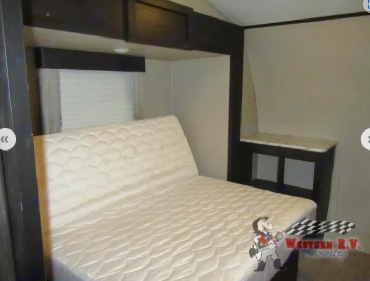 RV rental bedroom view: a comfortable mattress with a raised head, overhead cabinets, and a window. Your cozy sleeping space.. Keystone Impact 2019