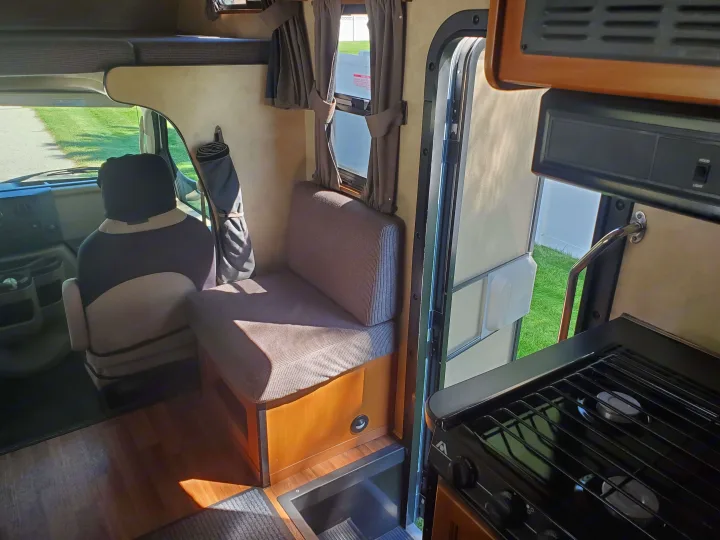 View inside an rv rental: driver's area, dinette bench, overhead bunk, and compact kitchen with stove. Functional and adventure-ready.. Thor Majestic 2014