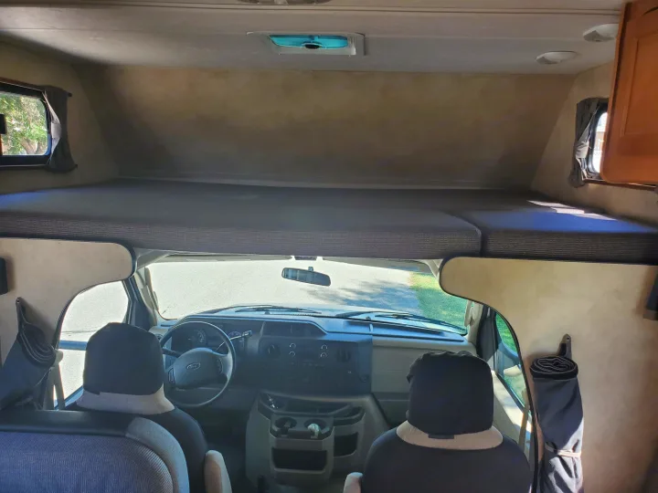 View of an RV rental's spacious interior: cab-over bunk bed above the cockpit area with driver/passenger seats.. Thor Majestic 2014