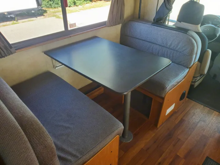 RV rental interior showing a dinette with grey fabric benches, a black table, window, and wood laminate floor.. Thor Majestic 2014
