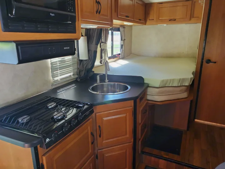 Compact RV rental interior featuring a kitchen with stove, sink, and microwave, alongside a comfortable bed area.. Thor Majestic 2014