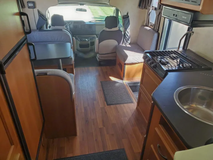 RV rental interior featuring a functional kitchen with stove and sink, a dining area, and the driving cockpit.. Thor Majestic 2014