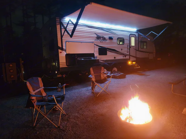 RV rental campsite at night: illuminated RV awning, two chairs, and a vibrant campfire create a cozy scene.. Jayco Jay Flight SLX 2019