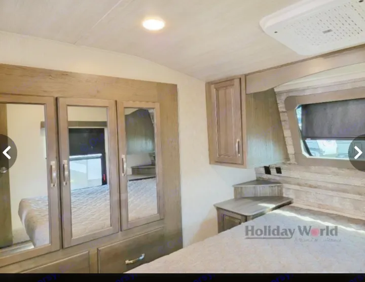 Spacious RV rental bedroom featuring a comfy bed, mirrored closet, overhead cabinets, and built-in nightstands.. Keystone Cougar 2023