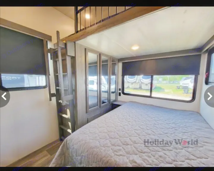 Spacious RV rental bedroom featuring a large bed, ladder to a cozy loft, and multiple windows with black blinds.. Keystone Cougar 2023