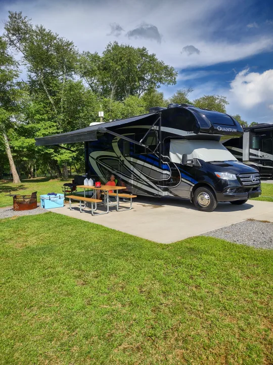 Relaxing at a sunny campsite with a Quantum rv rental, featuring an extended awning, picnic table, and outdoor amenities.. Thor Quantum 2021