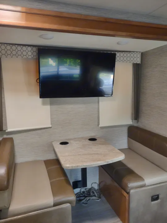 Spacious RV rental interior features comfortable dinette seating, table with cupholders, and wall-mounted TV.. Thor Quantum 2021