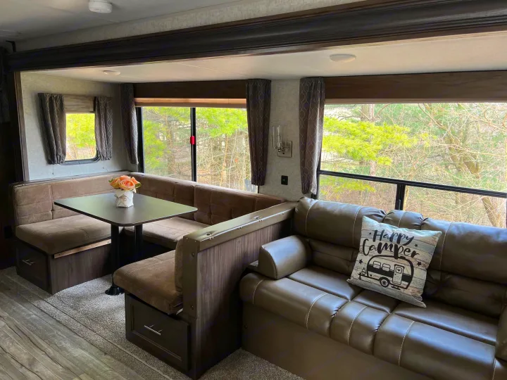 Spacious RV rental interior featuring a comfortable U-shaped dinette, sofa, and large windows with treed views for your next adventure.. Forest River Cherokee 2019