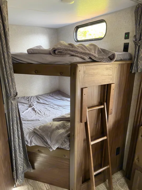 This RV rental features a cozy bunk bed setup with a window, ladder, and bedding, offering comfortable sleeping for travel.. Forest River Cherokee 2019
