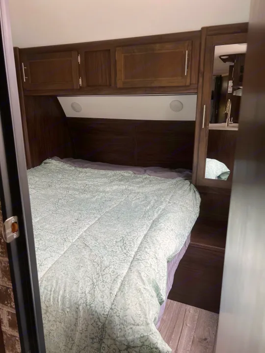 An inviting RV rental bedroom showing a bed with a green comforter, dark wood cabinets, and built-in mirrored storage.. Forest River Cherokee 2019