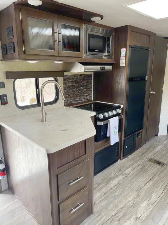 Modern RV rental kitchen with sink, microwave, stove, and fridge, showing ample counter space and storage.. Forest River Cherokee 2019