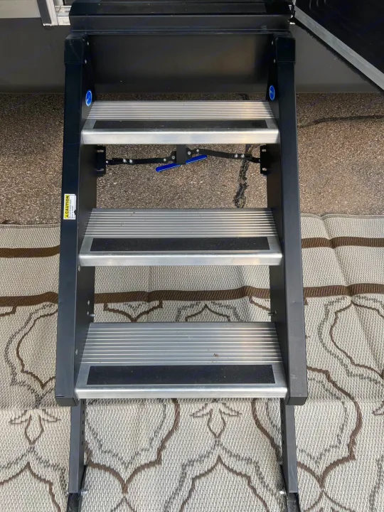 Three extended silver RV rental steps with black anti-slip strips rest on a patterned mat for easy access.. Forest River Cherokee 2019