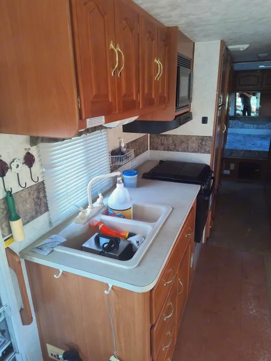 RV rental galley kitchen featuring wooden cabinets, double sink, stove, and microwave. Perfect for on-the-road cooking.. Damon Corporation Daybreak 2001