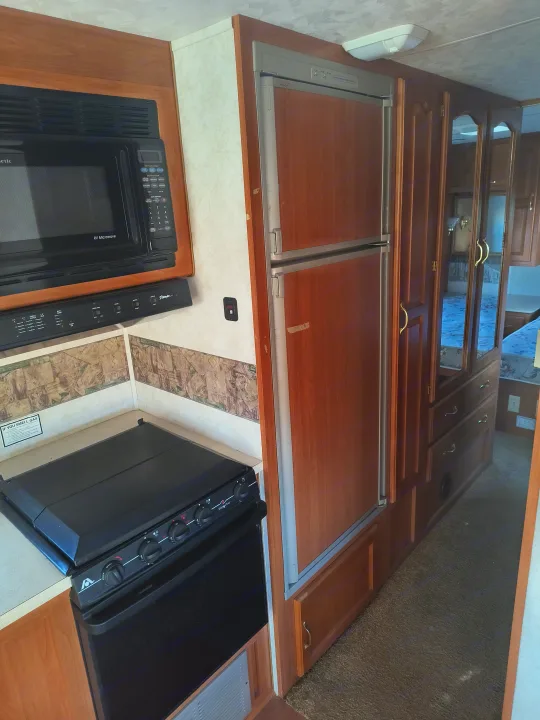 Inside this RV rental: a compact kitchen with a microwave, stove, and refrigerator. Beyond, mirrored doors reflect the bedroom.. Damon Corporation Daybreak 2001