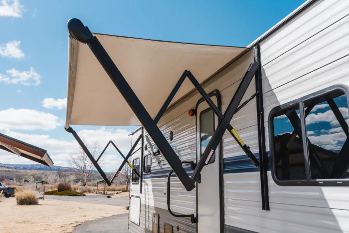 A white RV rental with a large, beige awning extended, providing shade at a sunny campground. Ideal for outdoor travel.. Gulf Stream Ameri-Lite 2021
