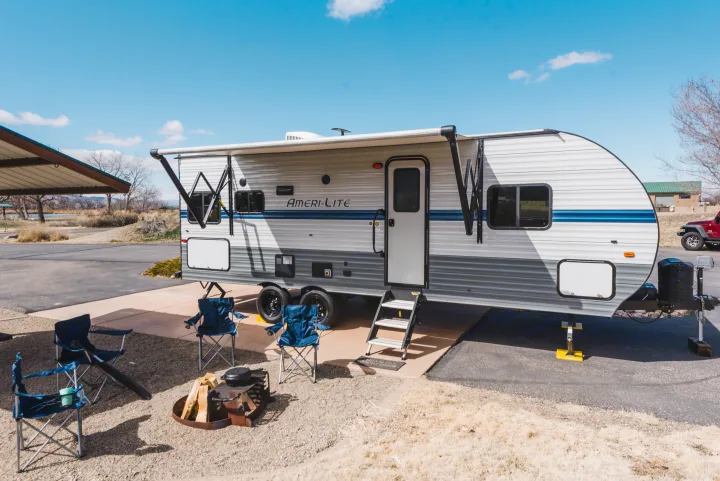 This Ameri-Lite travel trailer RV rental awaits adventures at a sunny campsite, complete with an awning, fire pit, & chairs.. Gulf Stream Ameri-Lite 2021