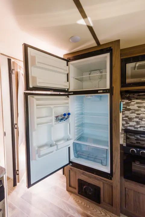 Clean rv rental kitchen with open two-door refrigerator, microwave, and stove, ready for your next adventure.. Gulf Stream Ameri-Lite 2021