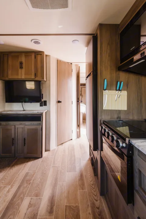 Bright RV rental interior showcasing a compact kitchen with oven, microwave, and fridge, opposite a living space with TV.. Gulf Stream Ameri-Lite 2021