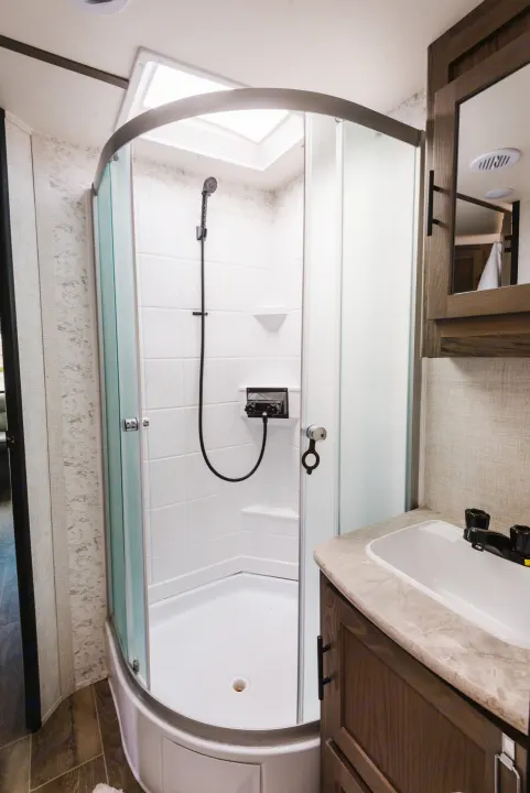 Spacious RV rental bathroom featuring a corner shower with a skylight, and a vanity with a sink.. Gulf Stream Ameri-Lite 2021