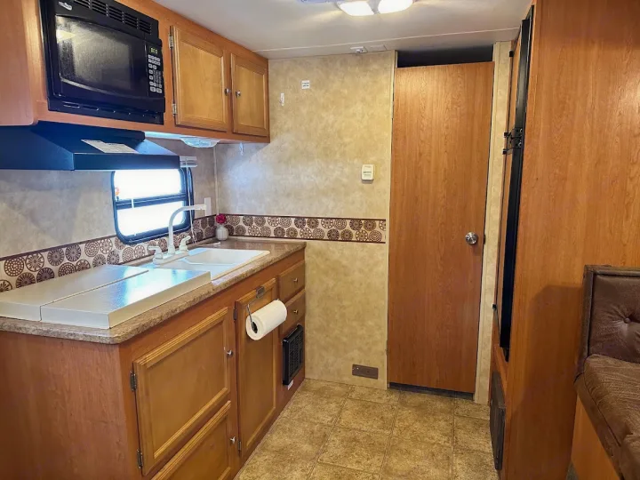 RV rental interior: a clean, functional kitchen with a microwave, sink, and light wood cabinets. Ideal for travel.. KZ Sportsmen 2009