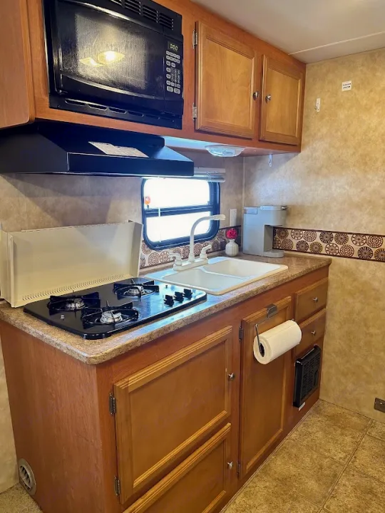 RV rental kitchen: Features include a microwave, gas stove, dual sink, and wooden cabinetry for a functional, travel-ready space.. KZ Sportsmen 2009