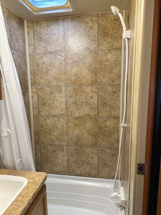 Compact RV rental bathroom featuring a shower, bathtub, and tiled walls with a skylight above.. KZ Sportsmen 2009